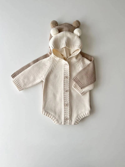 A beige cotton knitted hoodie romper with a teddy bear design, featuring a hood, sleeves, and a front pocket.