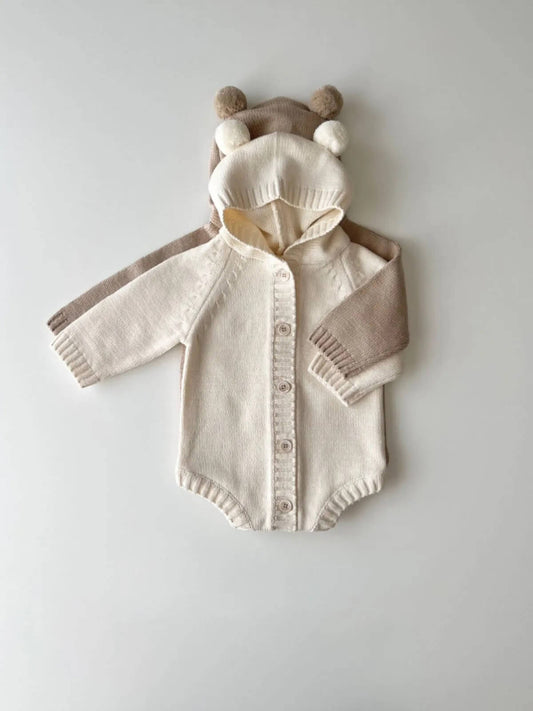 A beige cotton knitted hoodie romper with a teddy bear design, featuring a hood, sleeves, and a front pocket.